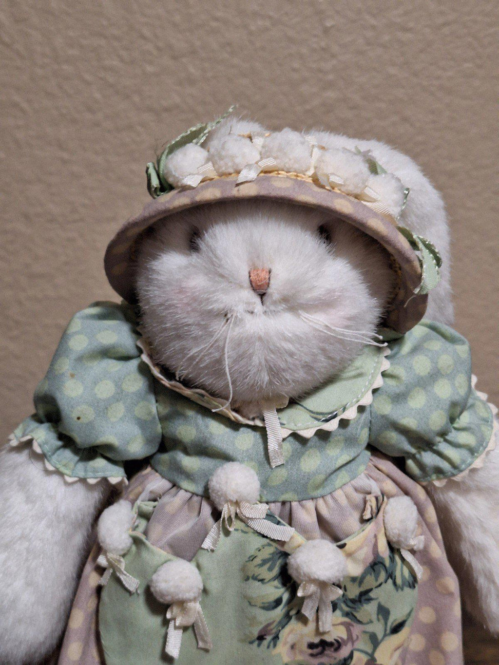 Close-up plush bunny face wearing a pastel bonnet and green floral ruffled outfit