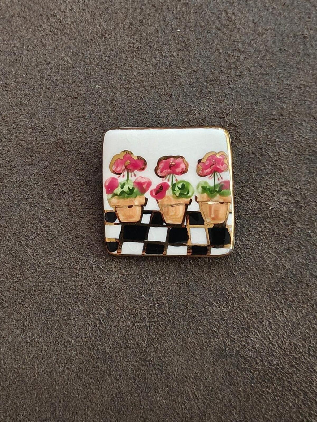 Square glazed ceramic brooch with pink flower pots arranged across a black checker pattern