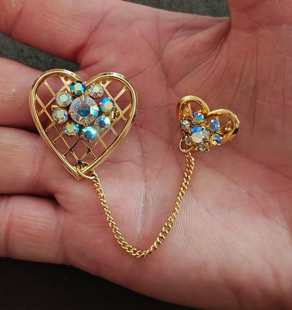 Gold-tone double heart brooch with blue iridescent rhinestones and dangling chain in hand