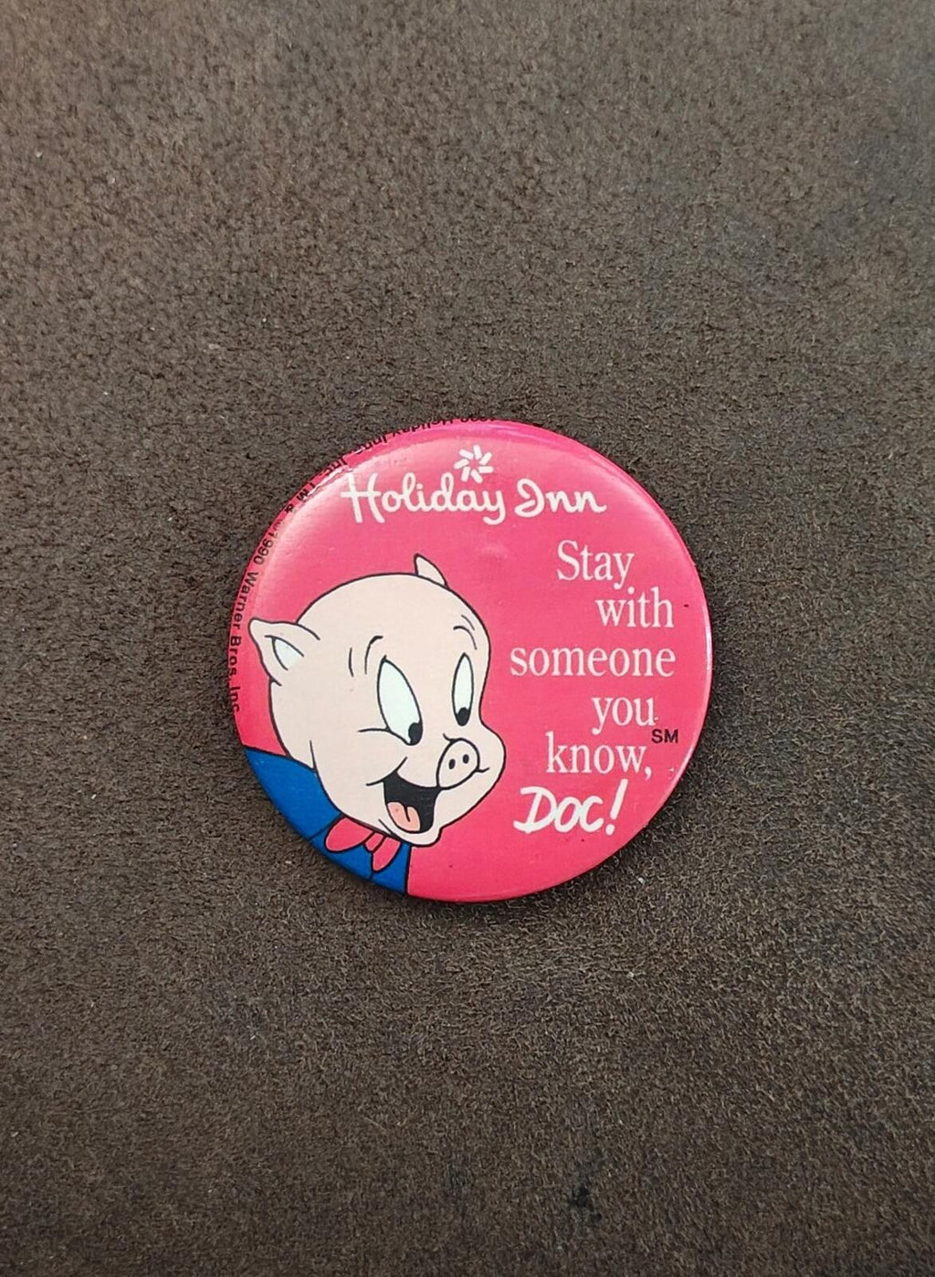 Pink button pin featuring Porky Pig and “Stay with someone you know, Doc!” on gray surface