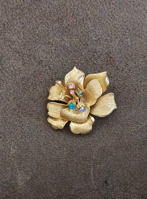 Gold-tone flower brooch with textured petals and blue rhinestone accents