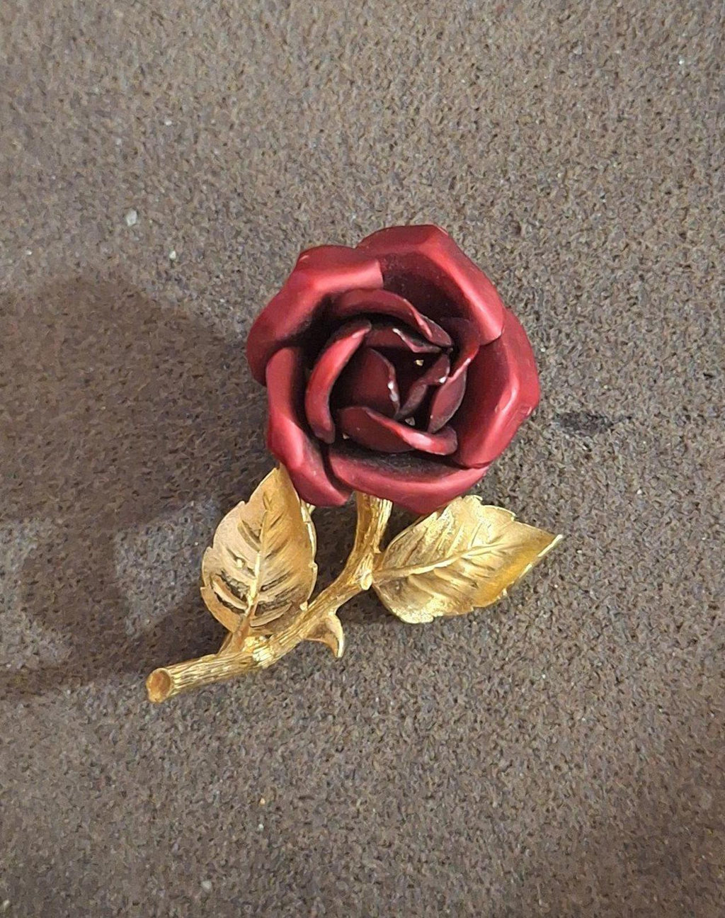 Gold-tone red rose enamel pin brooch with gold leaves and stem, front angled.
