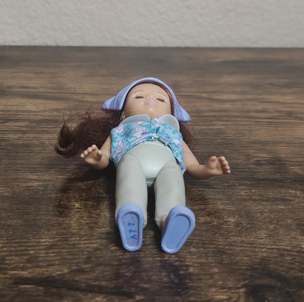 Madame Alexander doll lying down, blue cap, floral top, pale legs and blue shoes