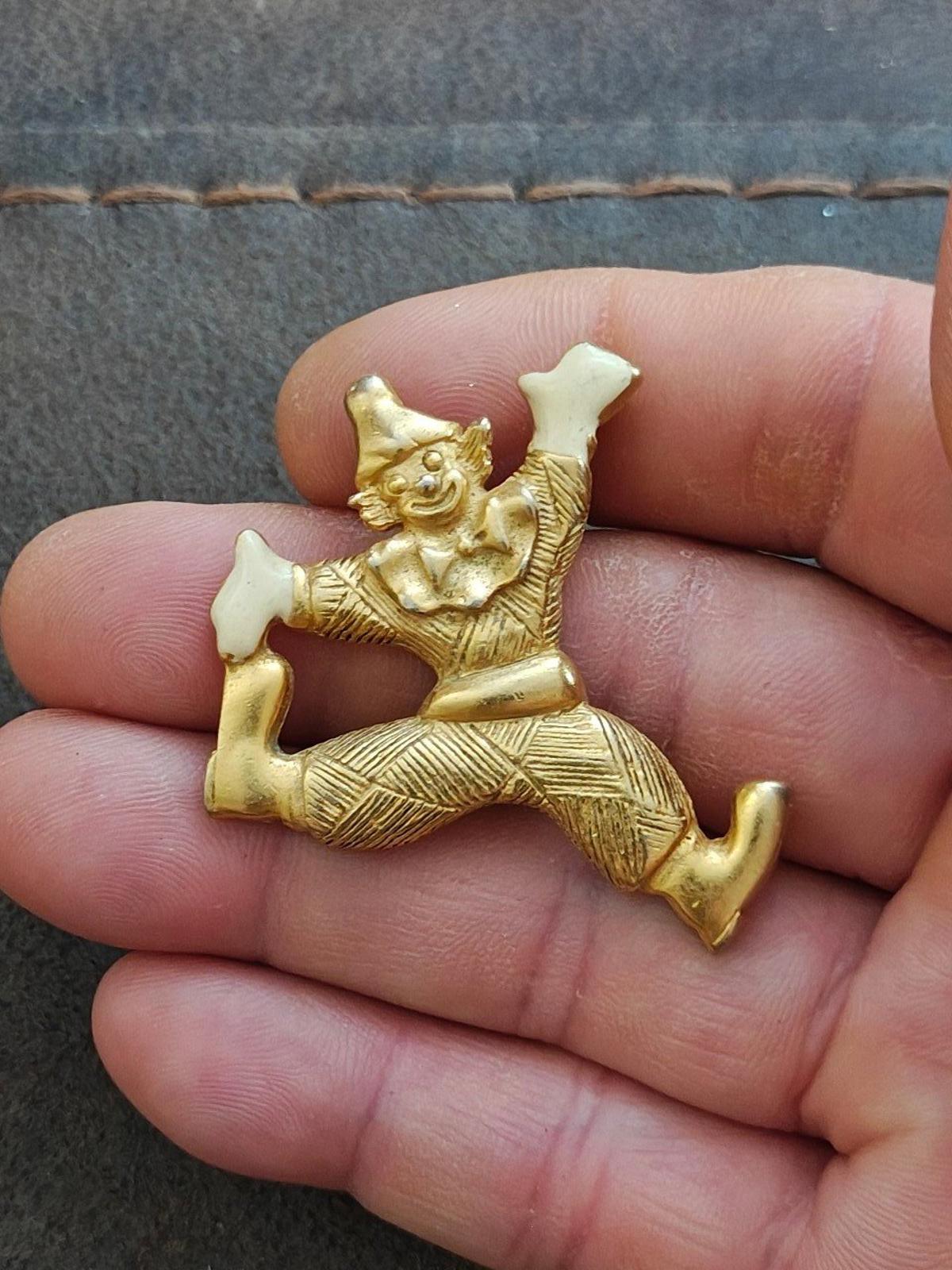 Gold tone clowning around enamel pendant with white enamel shoes and hands, close-up on fingertip