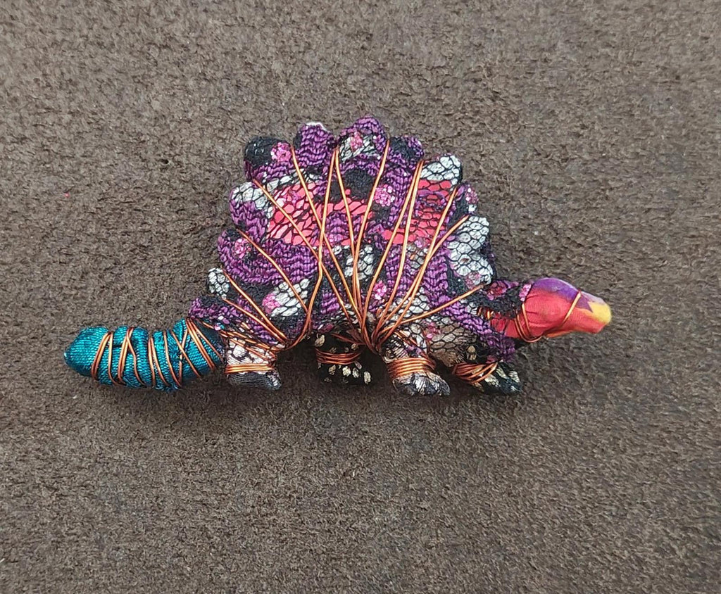 Purple stegosaurus dinosaur brooch on surface, beaded mosaic spikes and turquoise tail