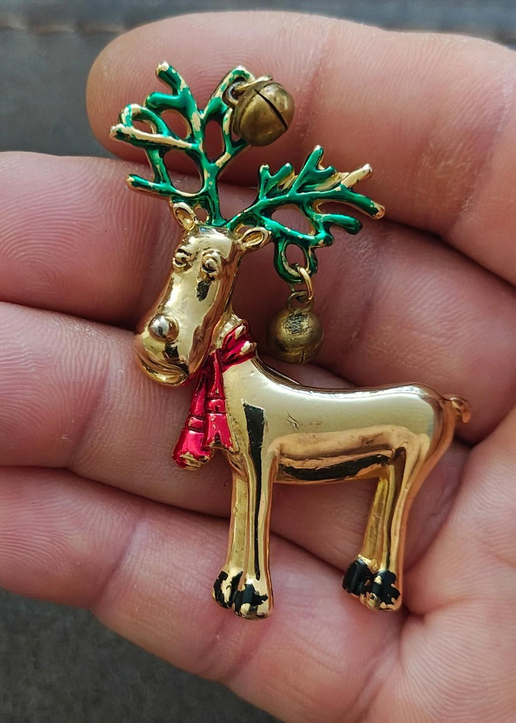 Gold-tone reindeer pin brooch in hand, green antlers, red scarf, and bells.