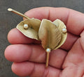 Gold leaf brooch with textured petals and faux pearl accents on a long pin