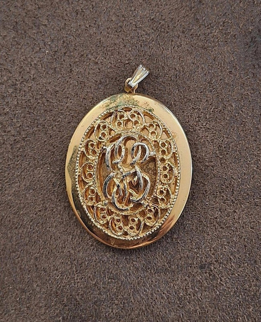 Gold tone oval filigree locket pendant with detailed ornate front motif and bail.