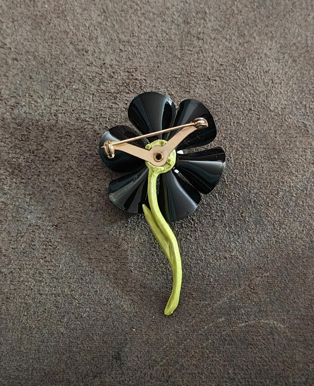 Black enamel flower brooch showing gold-tone pin and clasp, green curved stem