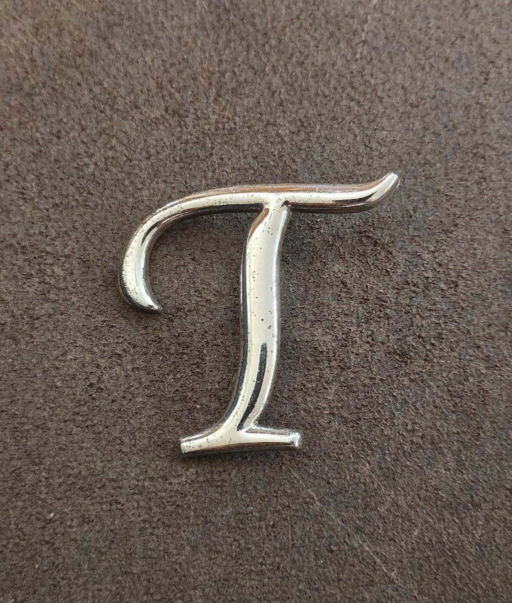 Silver-tone letter T pin/brooch, full letter shape visible, front view.