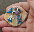 Enamel lapel pin with blue and purple little people and house scene, circular center