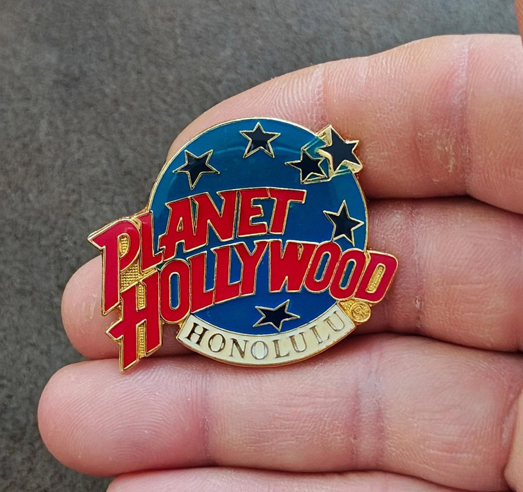 Planet Hollywood Honolulu enamel lapel pin held in hand, blue background with star accents
