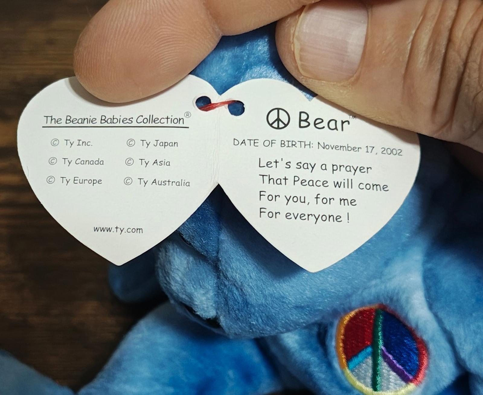 Blue bear plush back view with embroidered peace patch and paper tag on body
