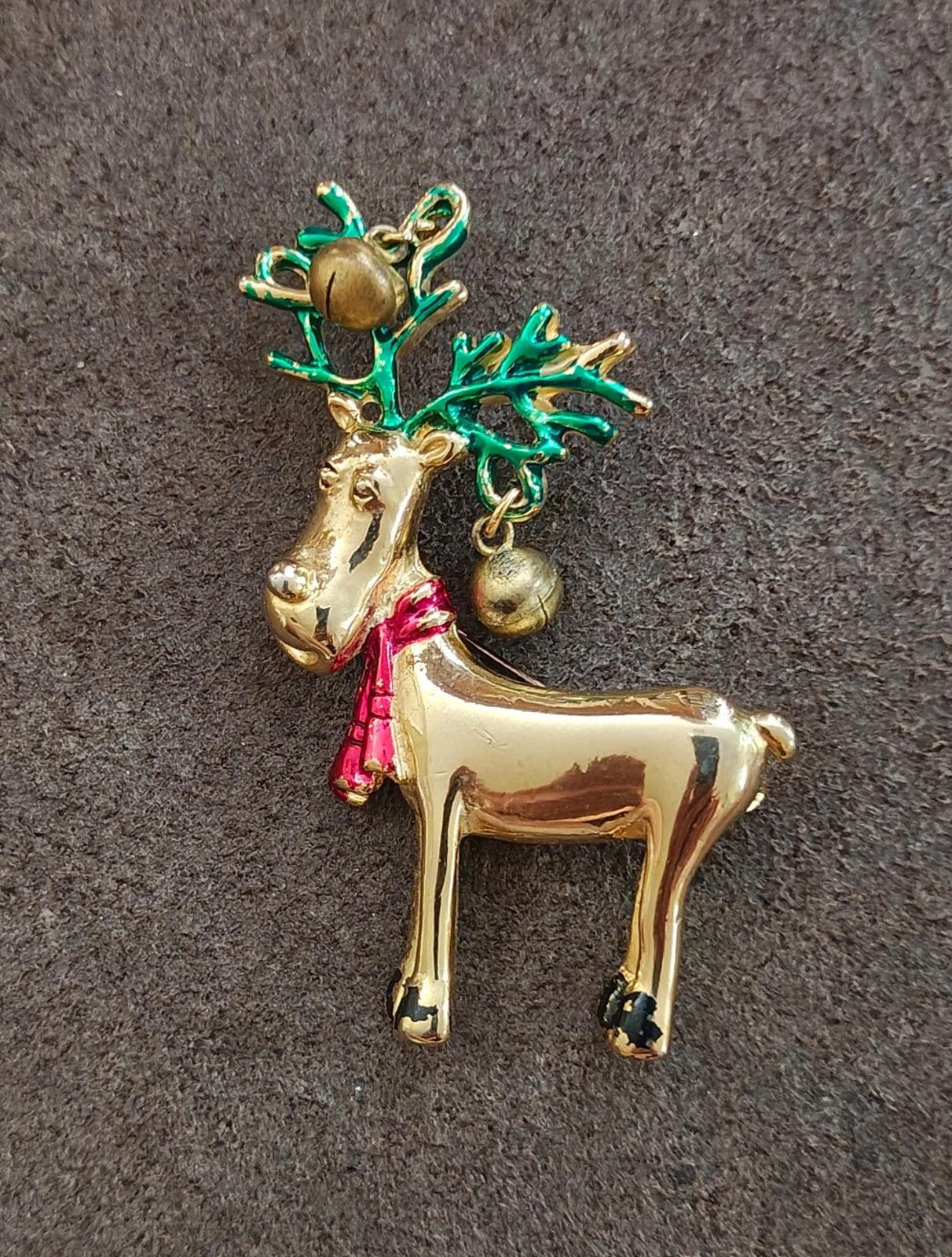 Gold-tone reindeer pin brooch on fabric, green antlers, red scarf, and bells.