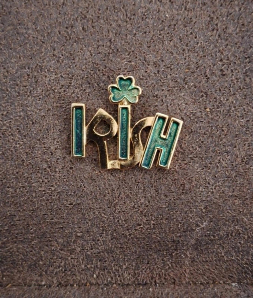 Gold-tone enamel Irish pin with green shamrock, on textured gray surface.
