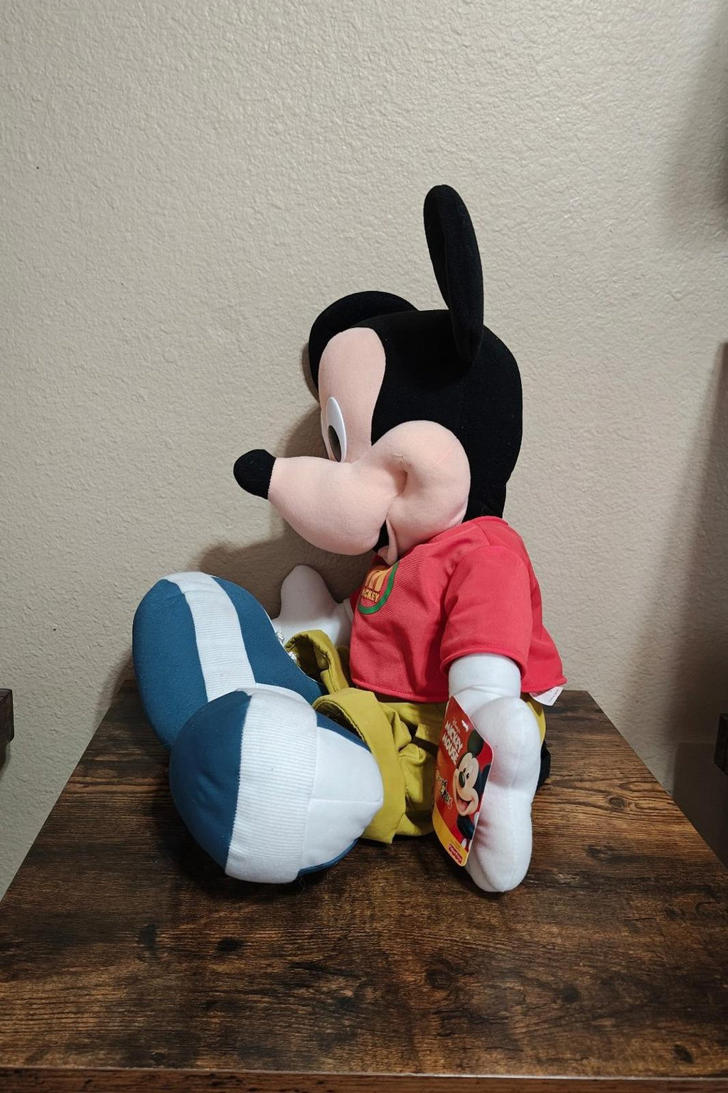 Mickey Mouse plush seated in profile wearing red shirt, yellow shorts, and blue shoes