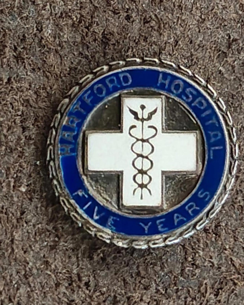 Close view of round hospital service enamel pin with blue enamel ring and white cross symbol