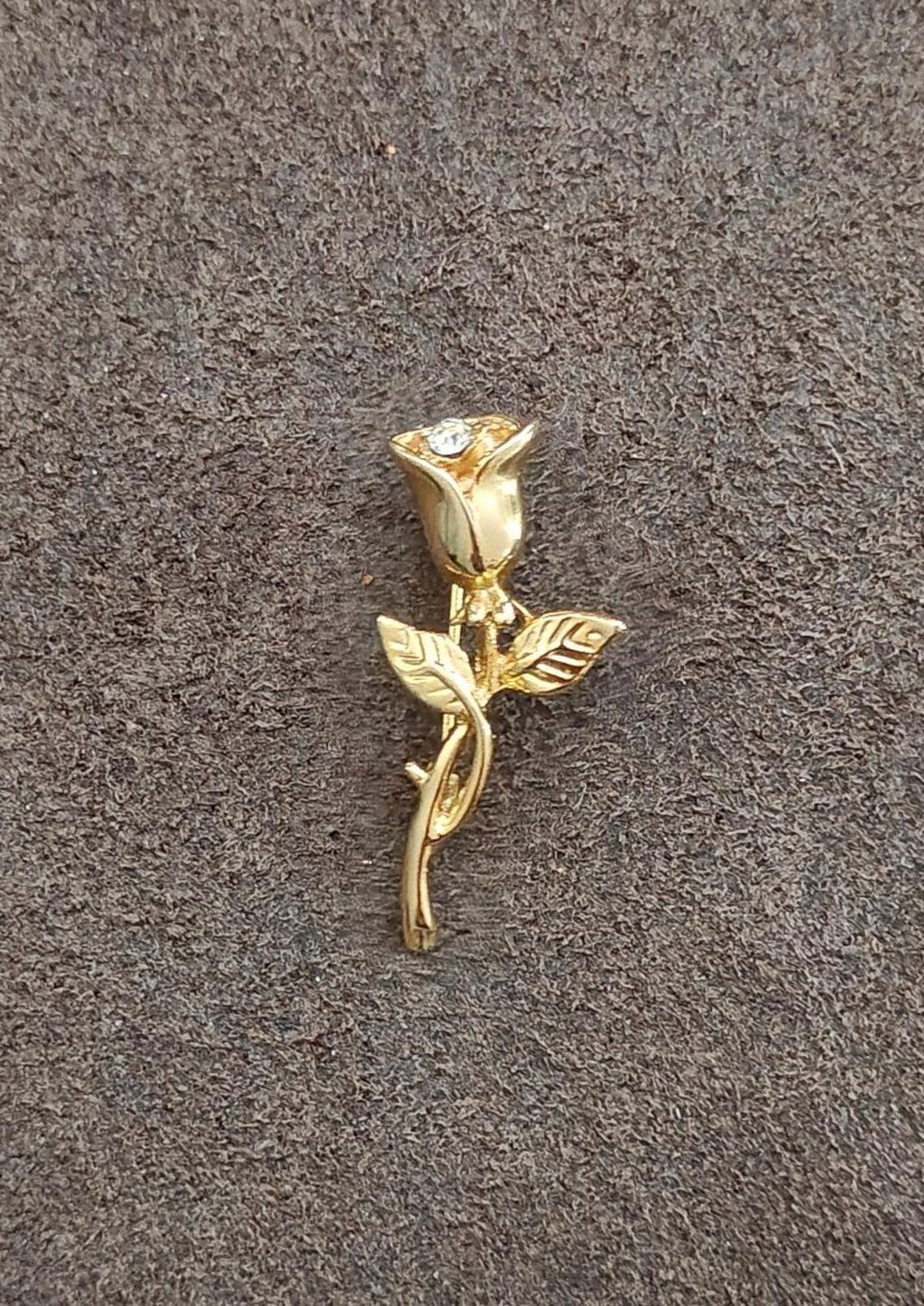 Gold-tone rose brooch with rhinestone center and leaf details, laid on fabric
