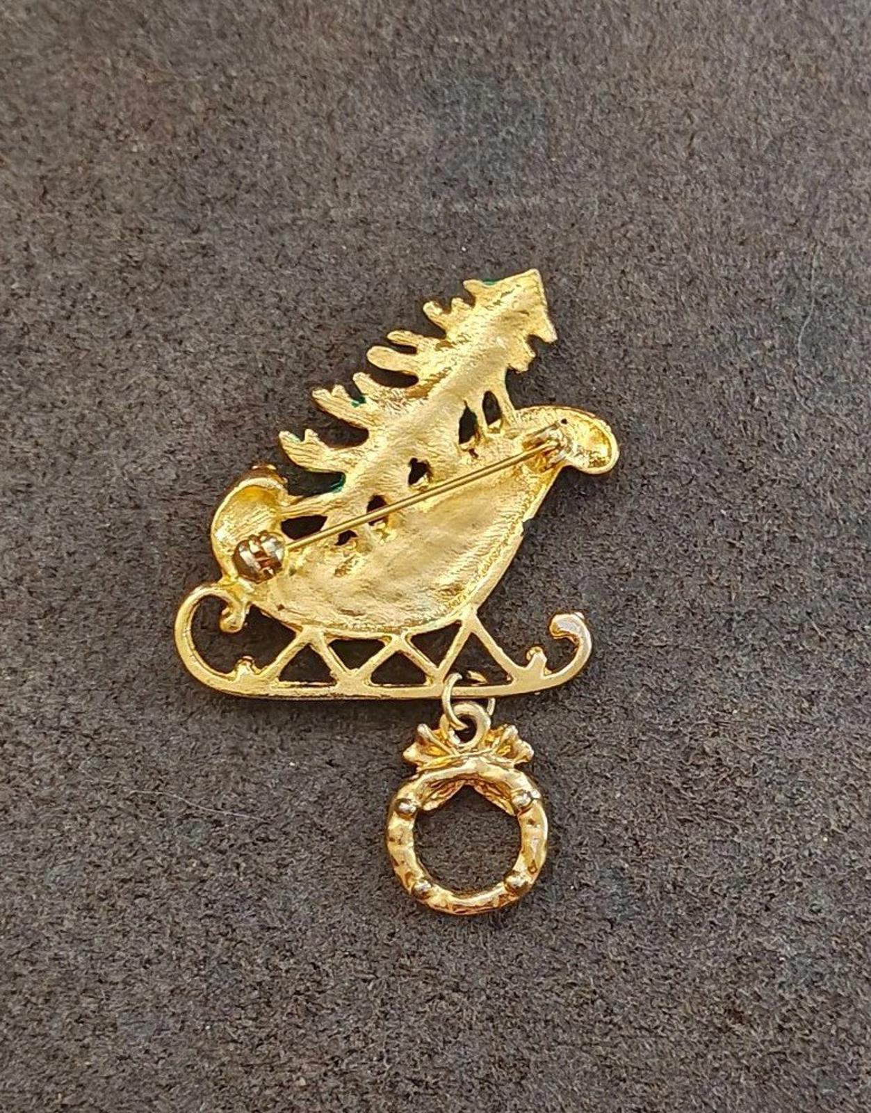 Gold-tone back of a Christmas sleigh enamel pin with hanging wreath charm loop.