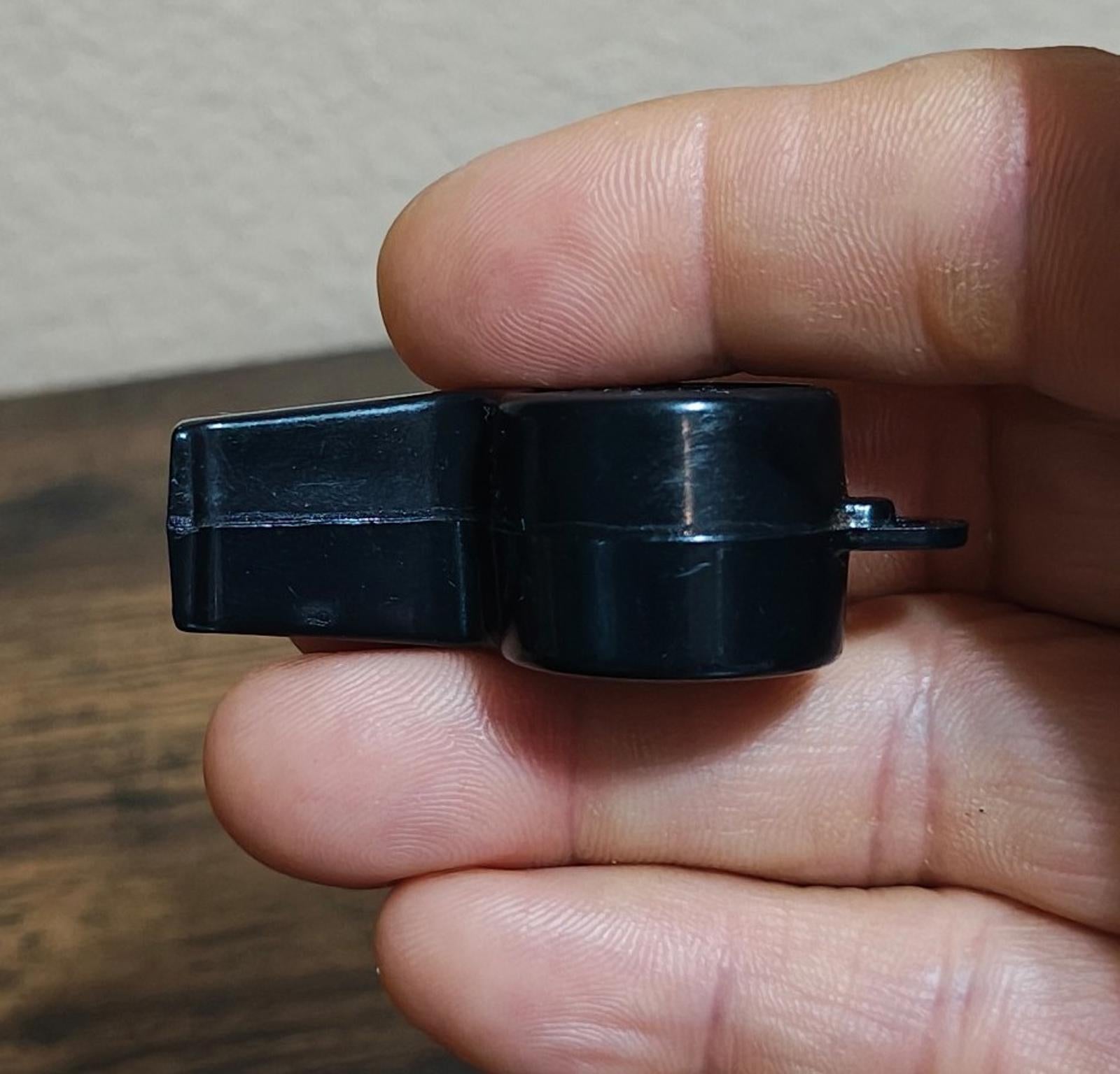 Black whistle with mounted loop and tube opening, side view in hand.
