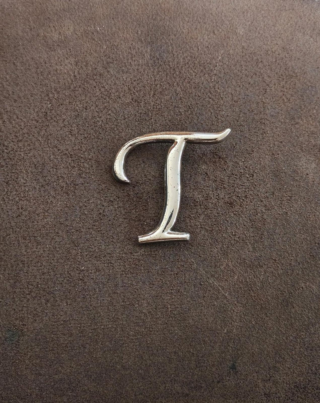 Silver-tone letter T pin/brooch with curved top and vertical center bar.