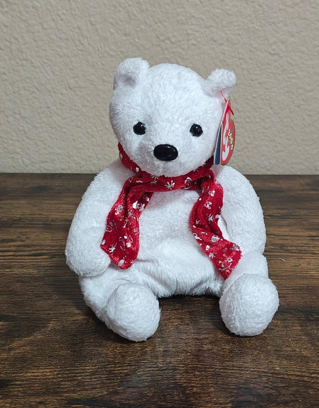 White bear plush sitting with red holiday scarf and small gift tag