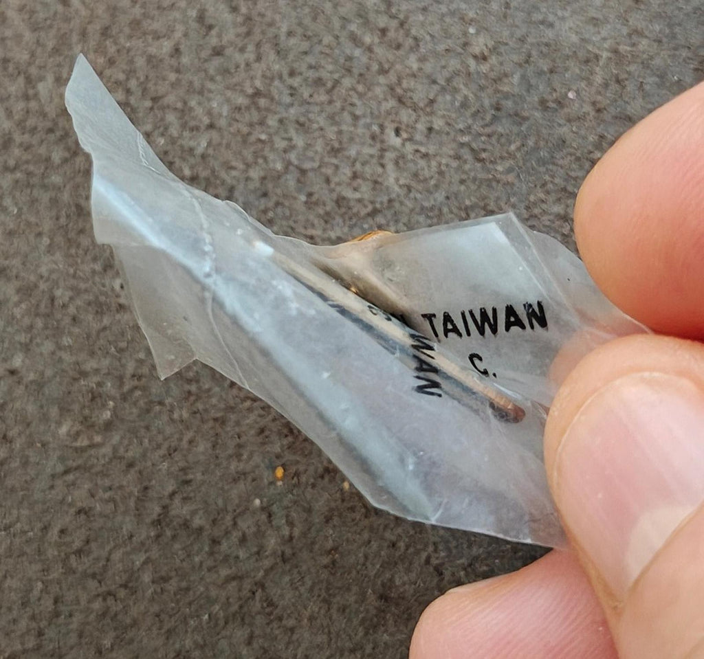 Gold-tone pin back showing "TAIWAN" marking and metal post, held in fingers
