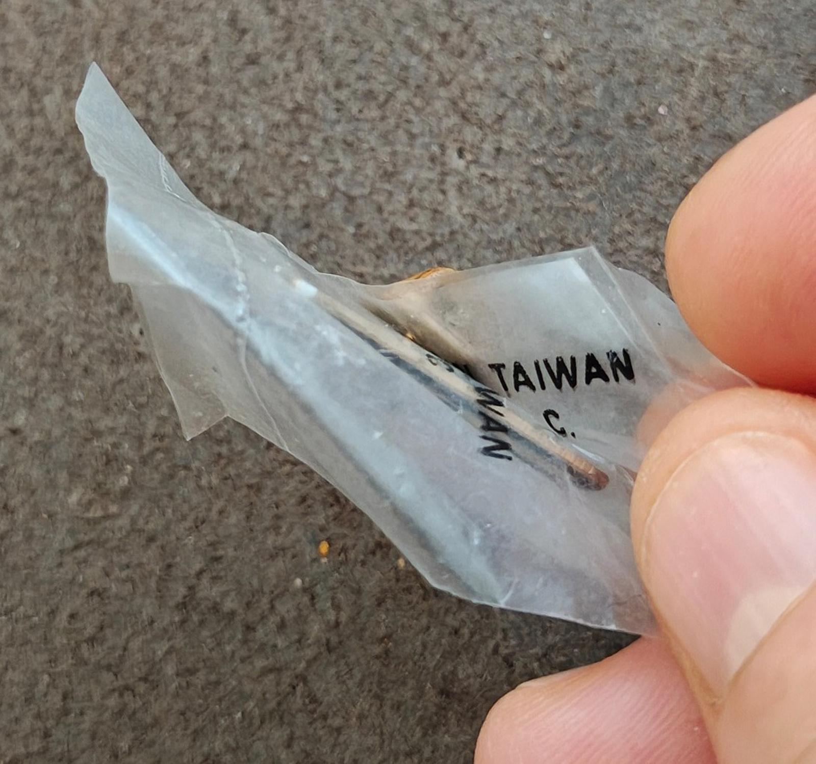 Gold-tone pin back showing "TAIWAN" marking and metal post, held in fingers