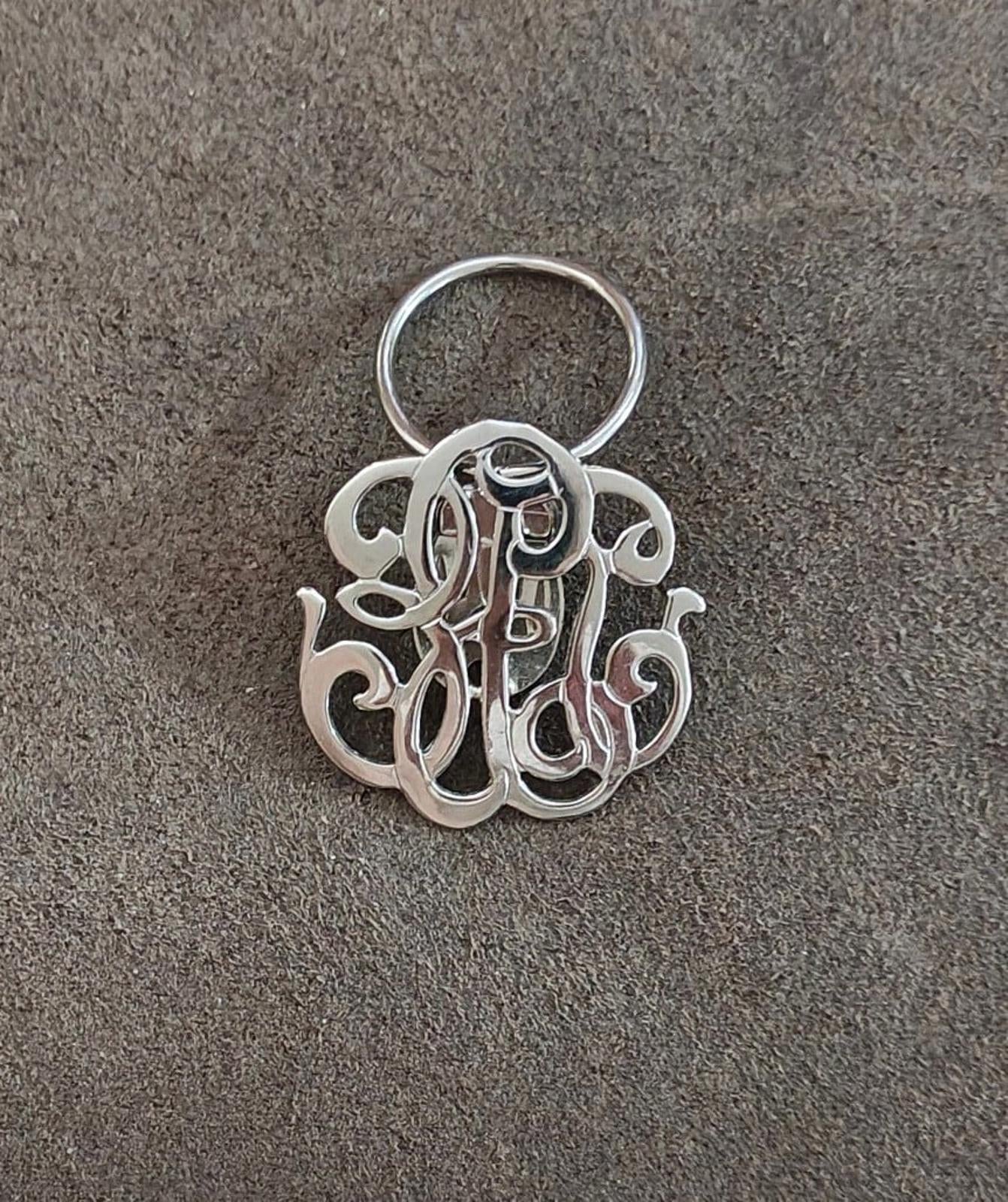 Silver-tone monogram scarf clip with circular ring at top and cutout letter design
