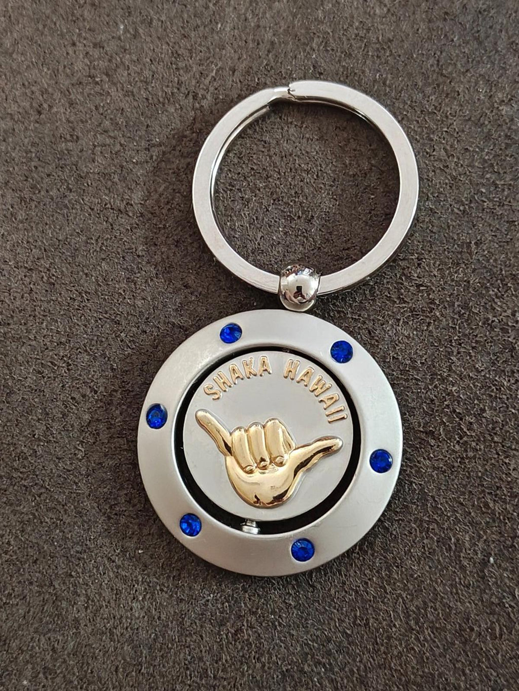 Two-tone round keyring with silver ring, blue jewel details, and gold Shaka Hawaii hand emblem.