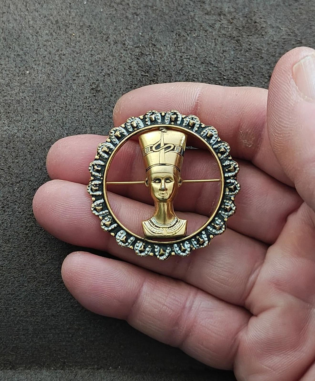 Gold-tone round brooch on hand, Nefertiti profile medallion with blue rhinestone border