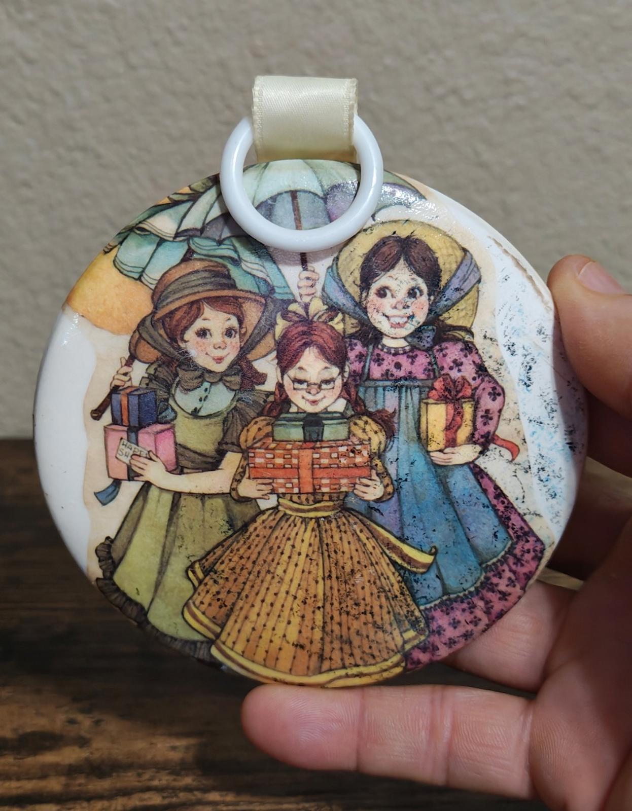 Round hanging ornament with illustrated three girls holding a small toy cart
