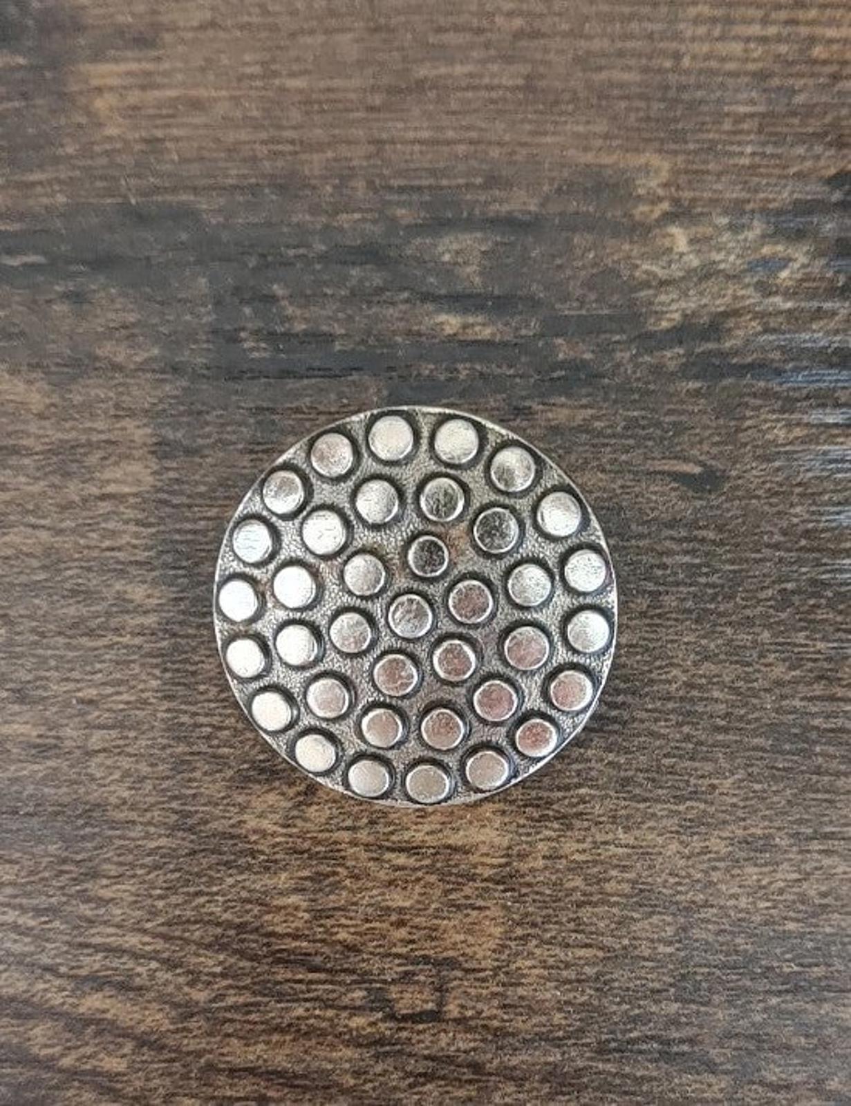 Round scarf clip with uniform raised dots on a silvery metal face