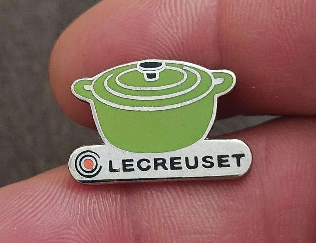 Le Creuset green mini cocotte enamel pin with silver-tone base, held up close