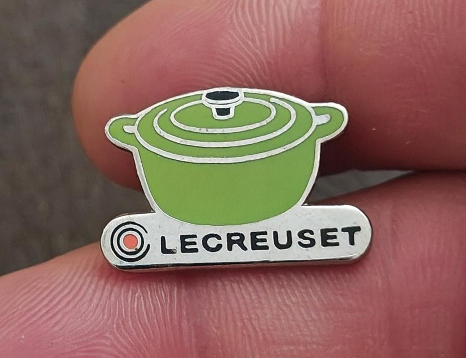 Le Creuset green mini cocotte enamel pin with silver-tone base, held up close