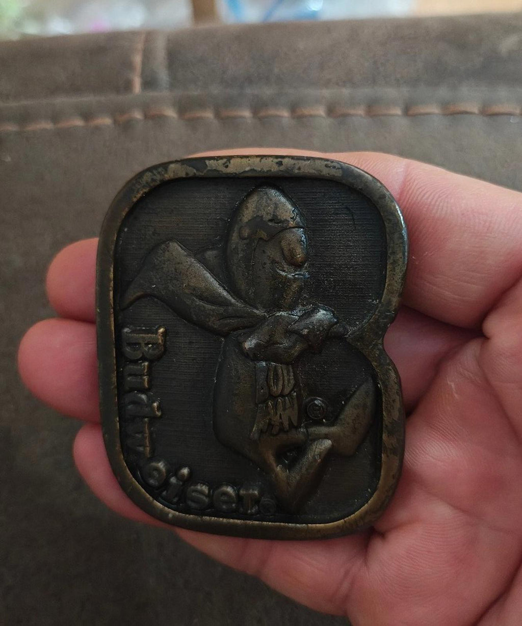 Vintage brass belt buckle held in hand, dark patina character front design with Budweiser text.