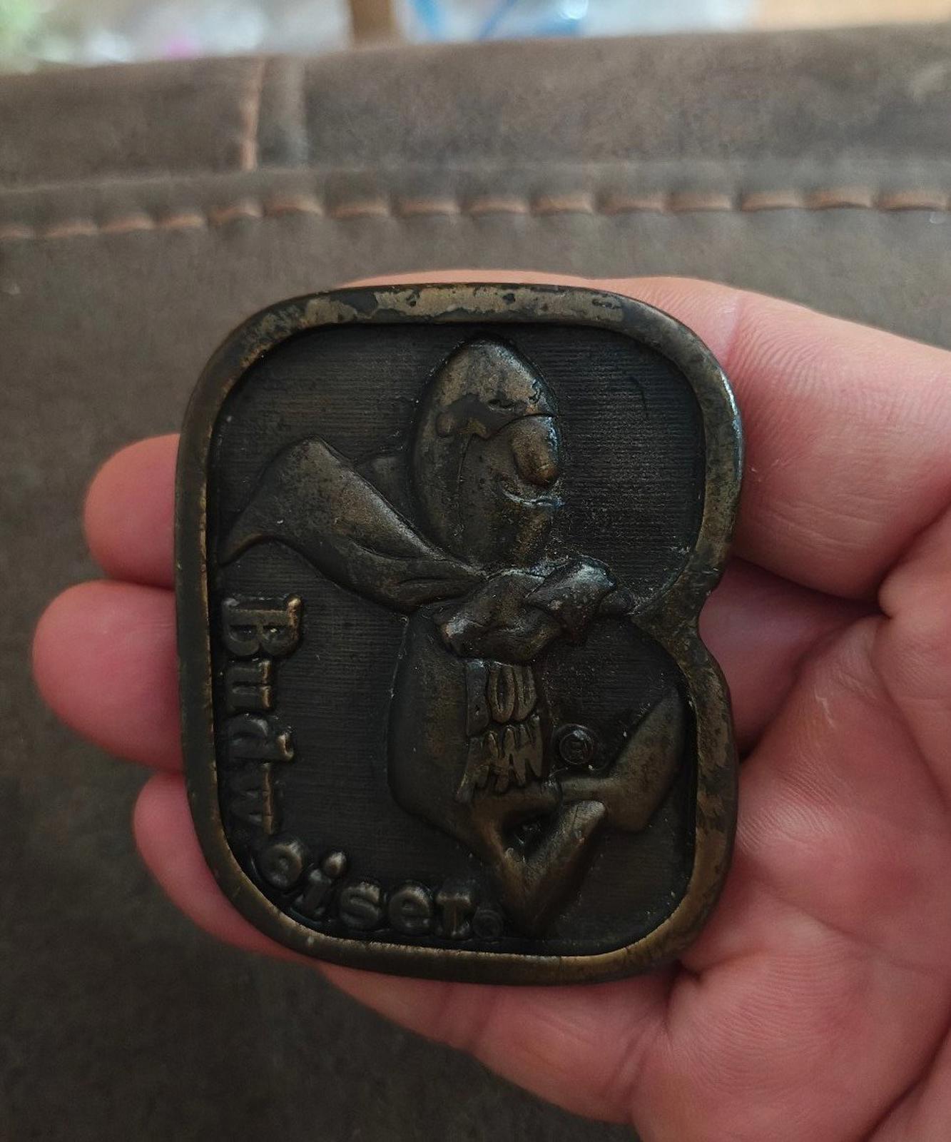 Vintage brass belt buckle held in hand, dark patina character front design with Budweiser text.
