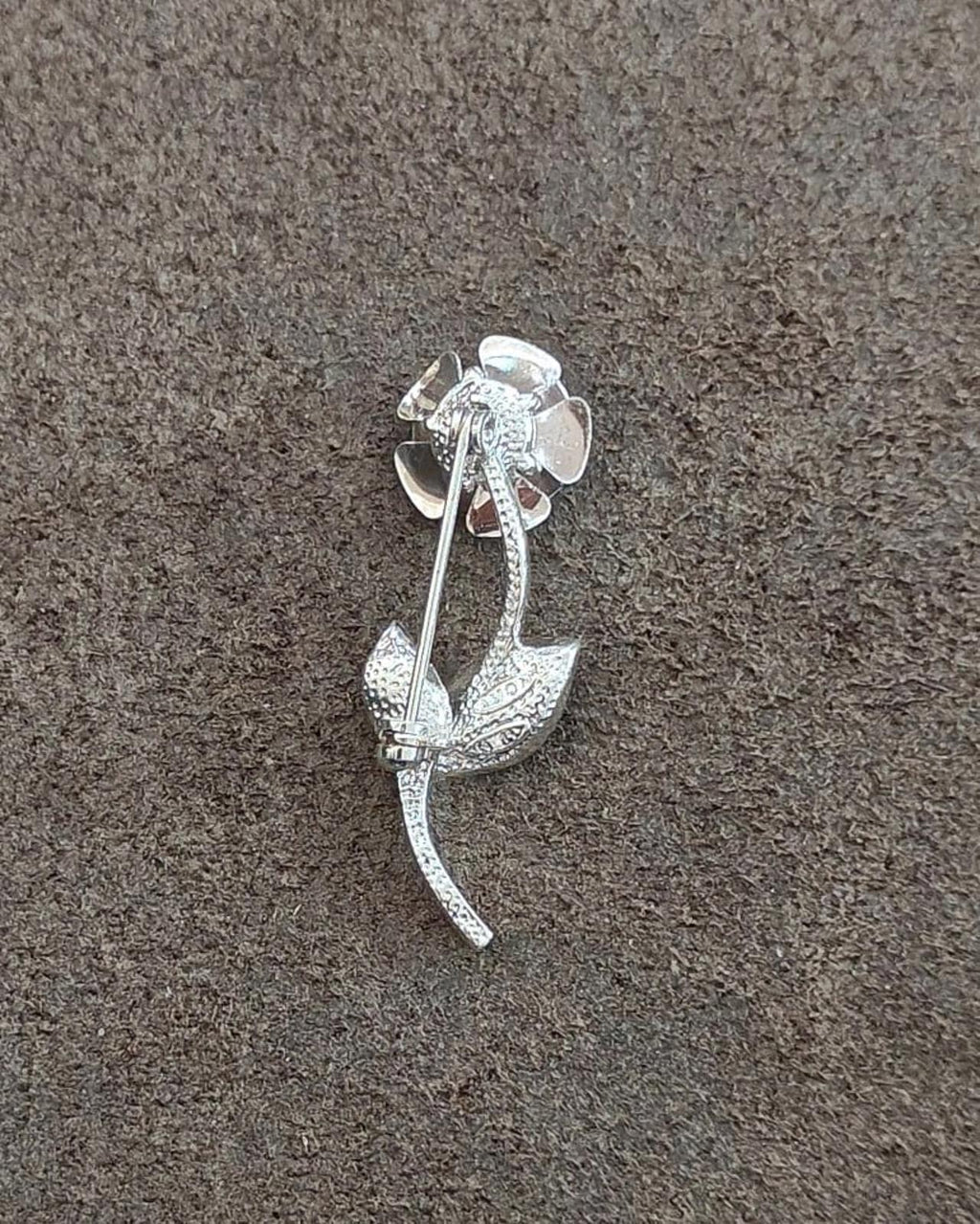 Silver-tone brooch with textured pin and rhinestone flower head, green enamel leaf
