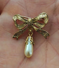Gold bow brooch with embossed scrollwork and a dangling faux teardrop pearl