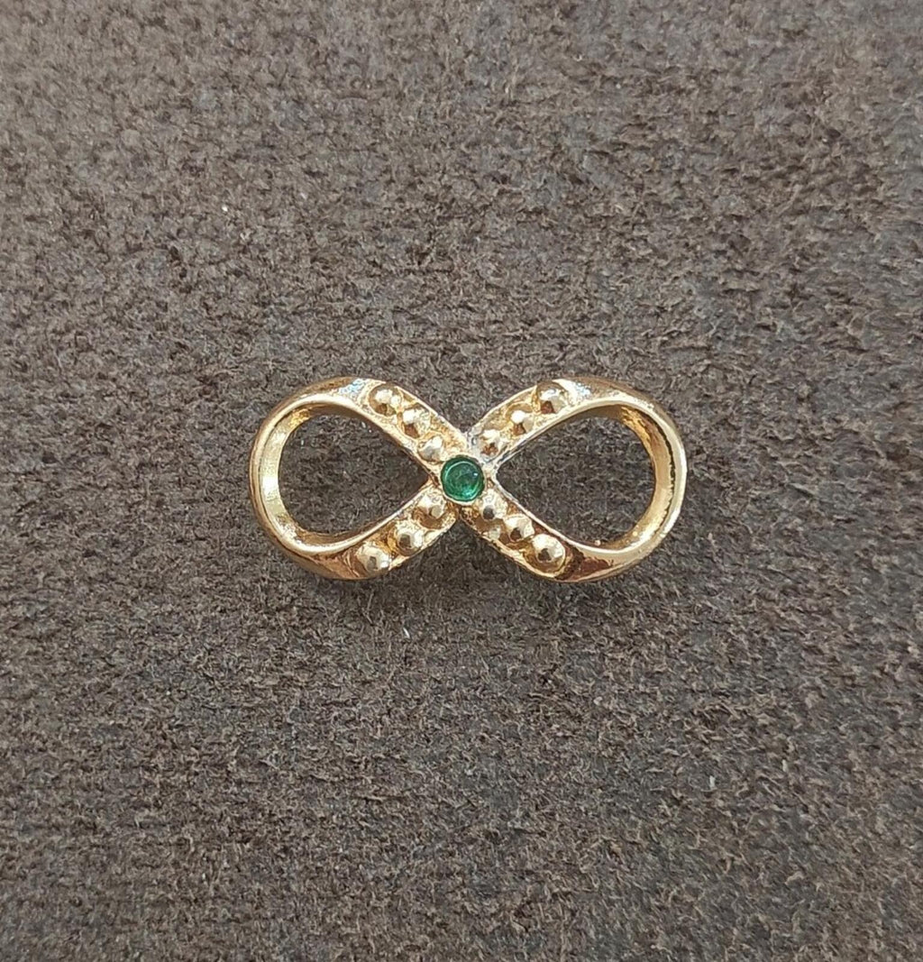 Gold infinity brooch with green emerald center and sparkling clear stone accents