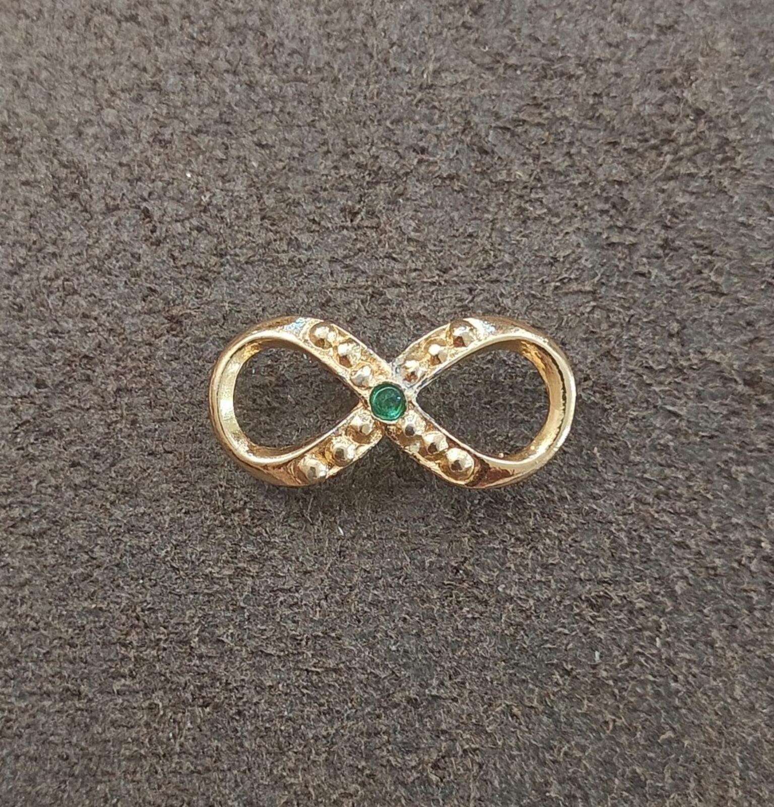 Gold infinity brooch with green emerald center and sparkling clear stone accents
