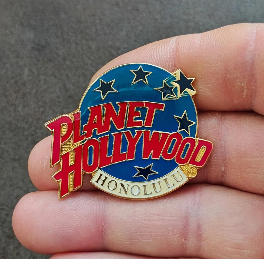 Planet Hollywood Honolulu enamel lapel pin held in hand, blue circle with stars and red logo