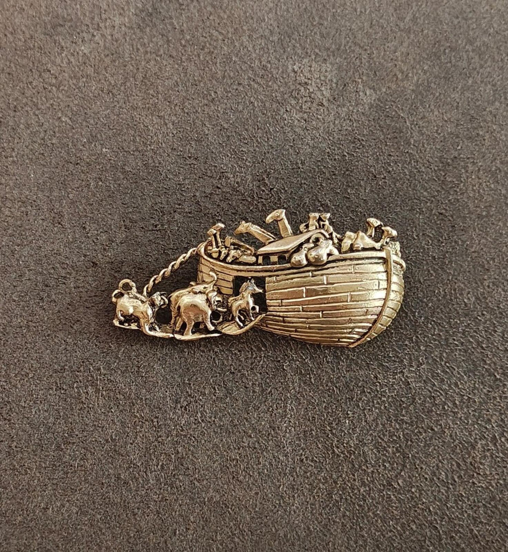 Gold tone Noah’s Ark brooch on dark fabric, angled view of boat and animals