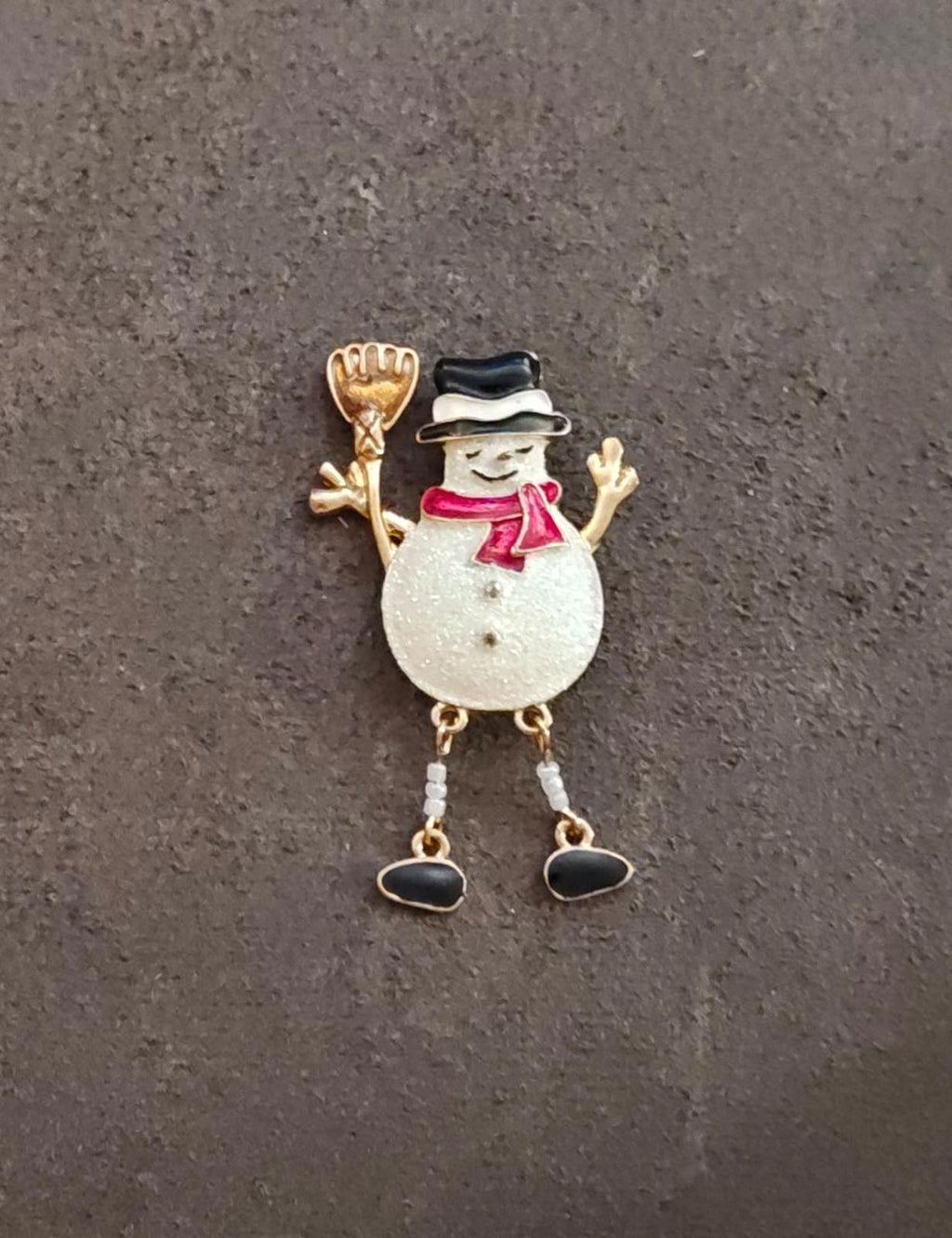 Gold tone snowman enamel brooch, white glitter body, red scarf, black top hat and dangling boots.