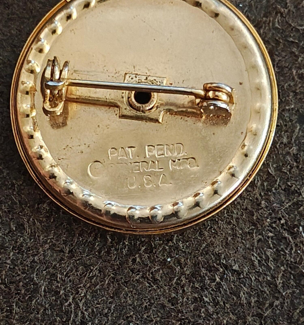 Gold-tone round brooch back showing pin hinge and PAT. PEND. text