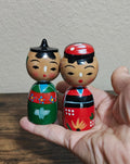 Pair of Japanese kokeshi wooden dolls, one green dress and one red dress, held in hand
