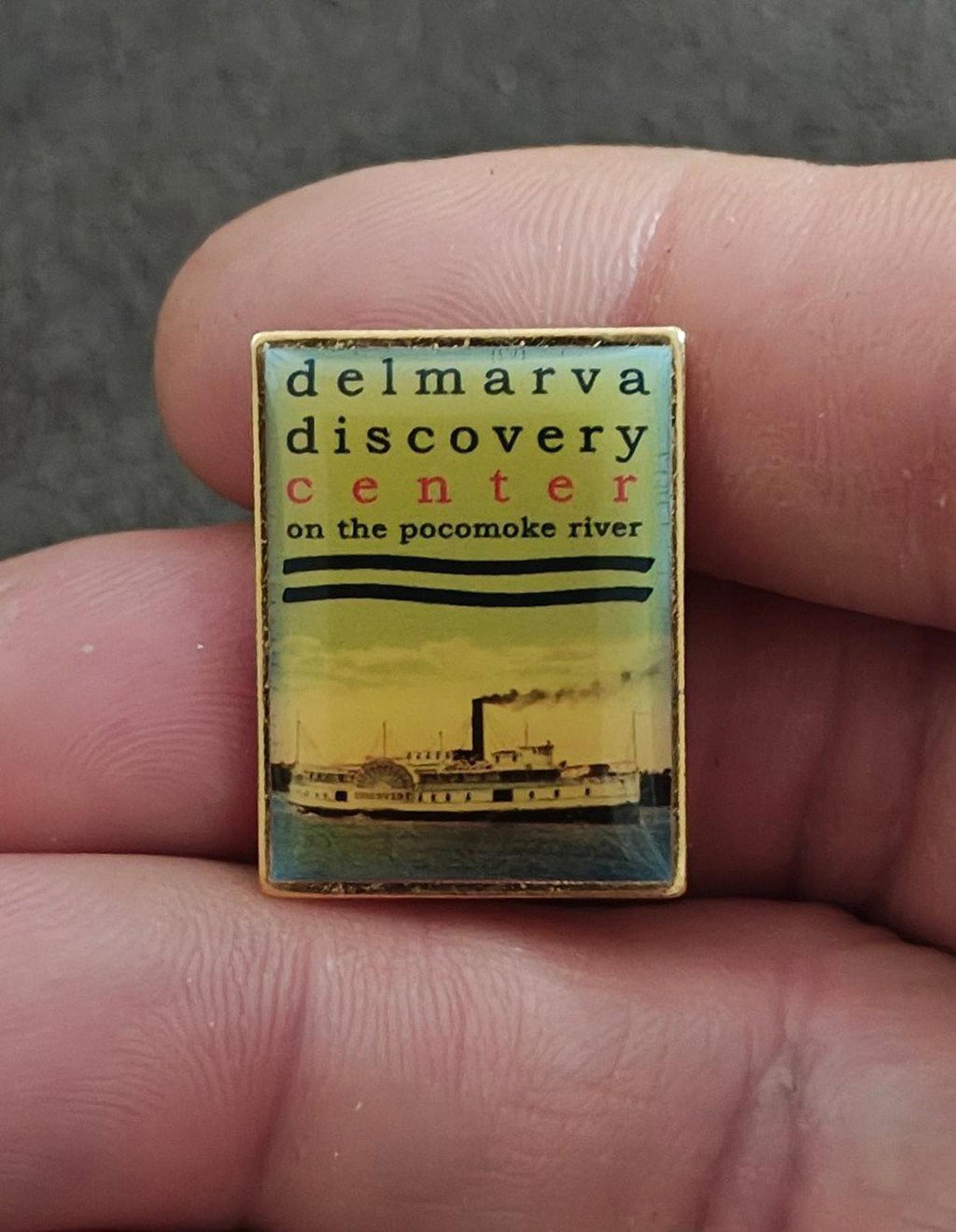 Gold Delmarva Discovery Center pin with ship graphic and multicolor text