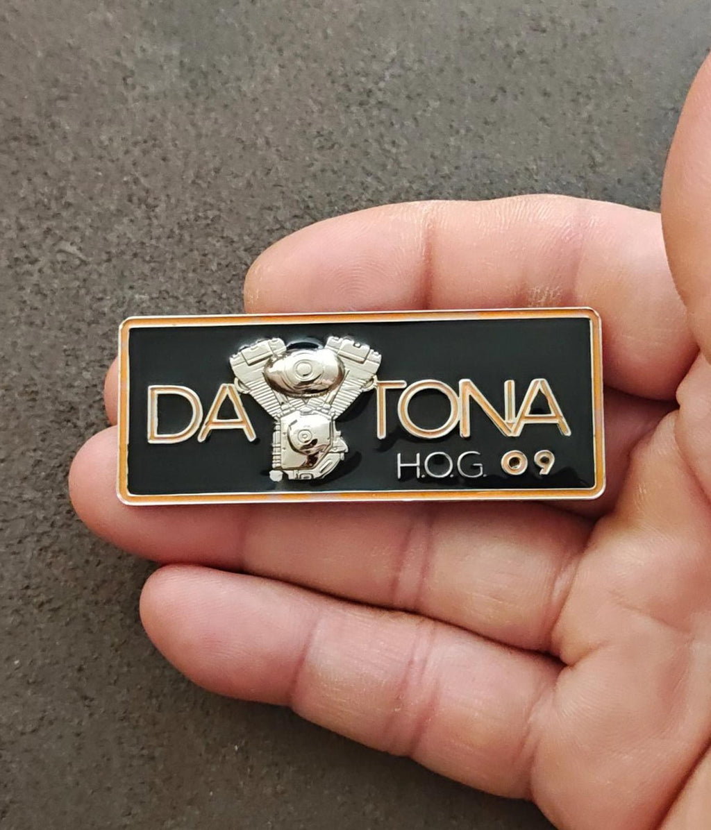 Black enamel Daytona H.O.G.09 pin with silver eagle emblem and gold border, held.
