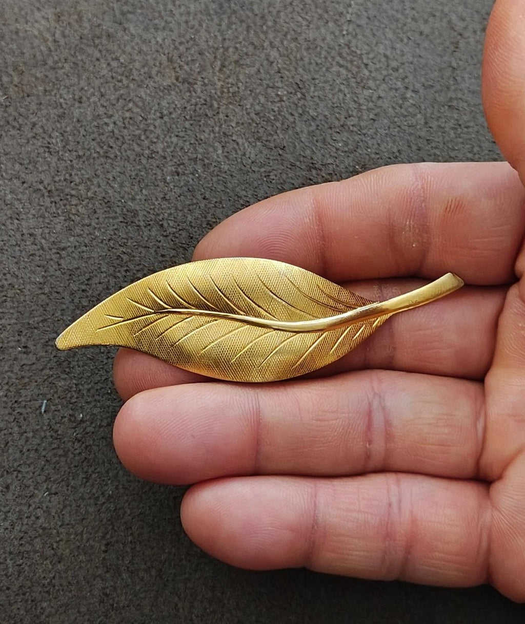 Gold-tone textured leaf brooch pin with raised leaf veins held in hand