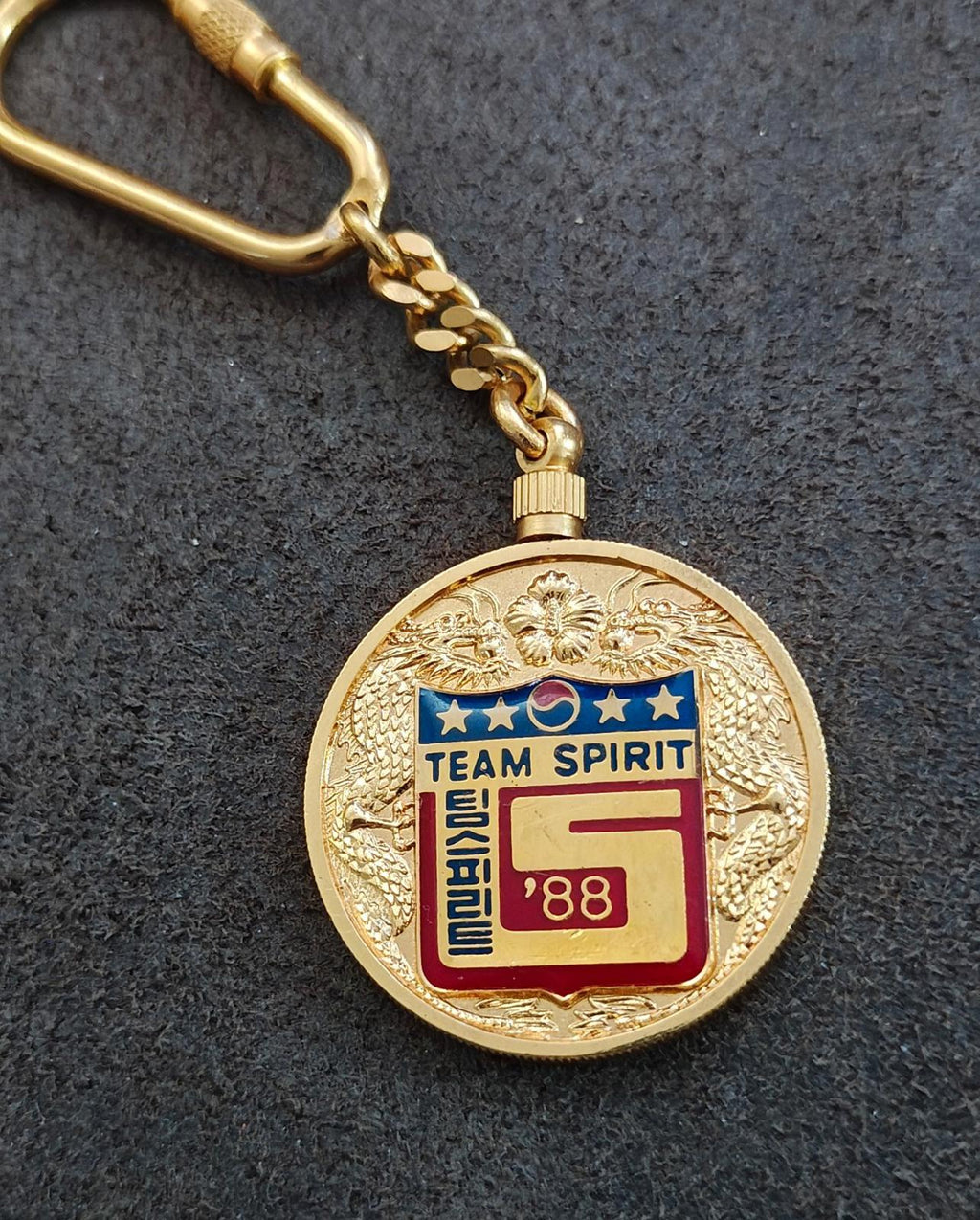 Gold round Team Spirit 1988 keychain medallion with chain and blue-red logo